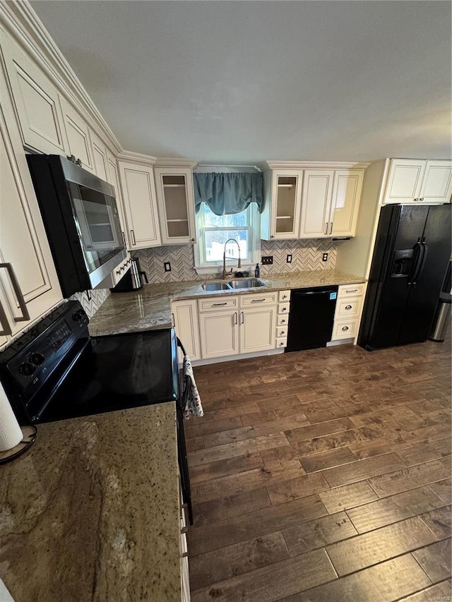 kitchen with tasteful backsplash, glass insert cabinets, dark wood-style flooring, black appliances, and a sink