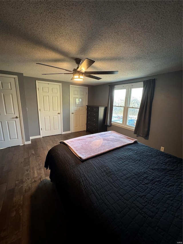 bedroom with a textured ceiling, ceiling fan, dark wood-style flooring, and baseboards