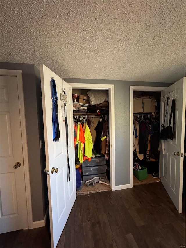 unfurnished bedroom featuring a textured ceiling, baseboards, multiple closets, and wood finished floors