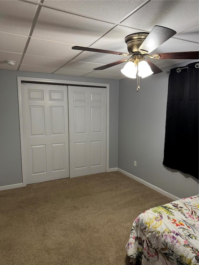 unfurnished bedroom with ceiling fan, a paneled ceiling, carpet floors, baseboards, and a closet