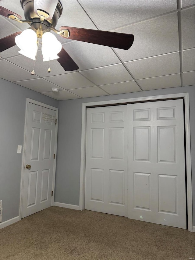 unfurnished bedroom with a paneled ceiling, carpet, baseboards, and a closet