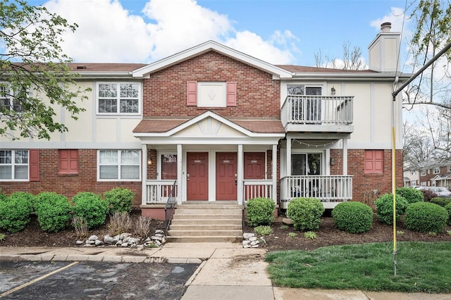 view of front of home with brick siding, a balcony, a chimney, a porch, and stucco siding