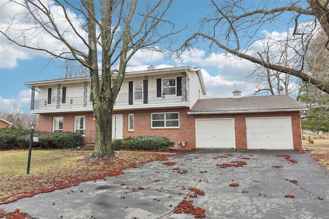 colonial-style house with a garage, a balcony, a chimney, aphalt driveway, and brick siding