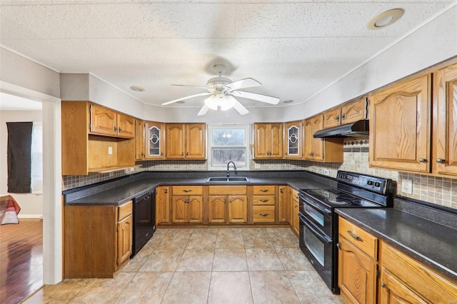 kitchen featuring brown cabinets, dark countertops, a sink, under cabinet range hood, and black appliances