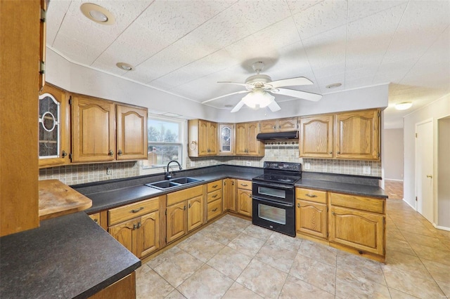 kitchen with range with two ovens, dark countertops, brown cabinets, under cabinet range hood, and a sink