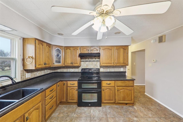 kitchen with under cabinet range hood, a sink, double oven range, tasteful backsplash, and brown cabinetry