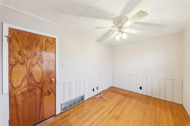 unfurnished room with a ceiling fan, a wainscoted wall, visible vents, and hardwood / wood-style floors