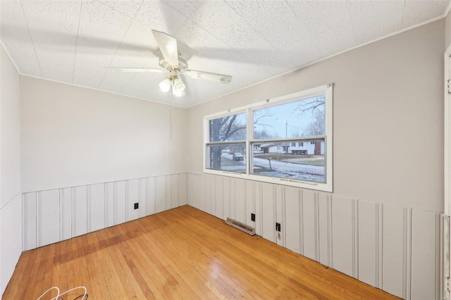 spare room featuring light wood-style floors, a ceiling fan, visible vents, and a wainscoted wall