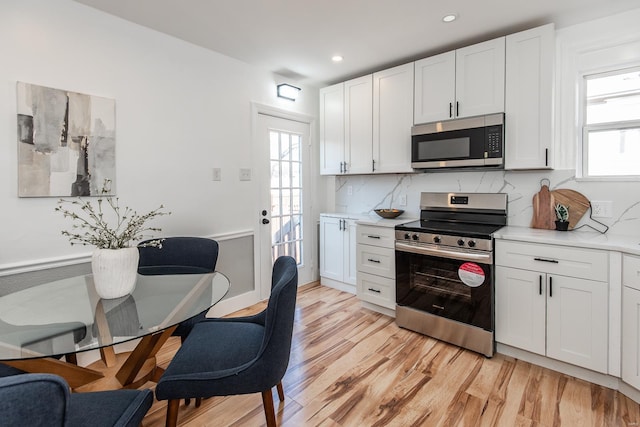 kitchen featuring stainless steel appliances, backsplash, light wood-style flooring, and light countertops