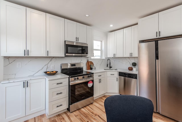 kitchen with white cabinetry, backsplash, light wood-type flooring, and appliances with stainless steel finishes