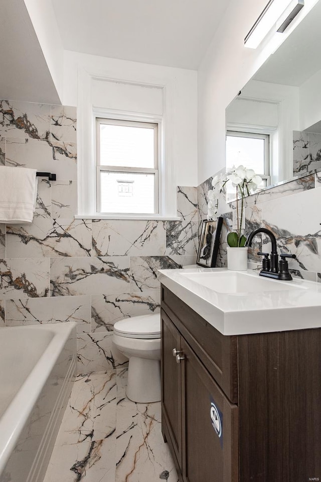 bathroom with toilet, marble finish floor, a bathing tub, tile walls, and vanity