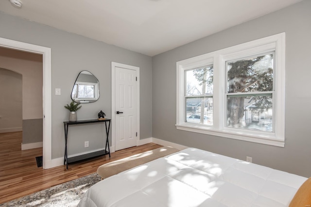 bedroom with arched walkways, visible vents, baseboards, and wood finished floors