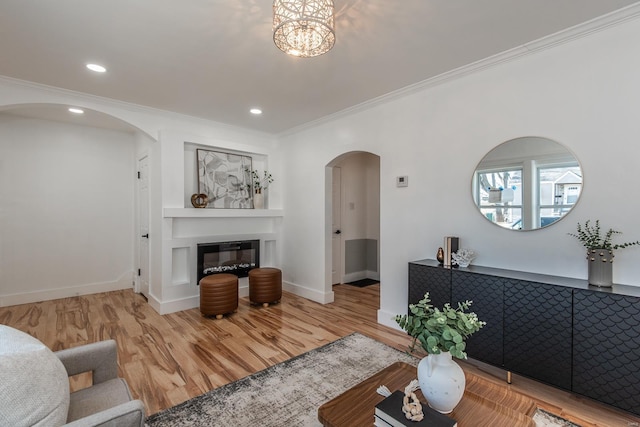 living room featuring wood finished floors, arched walkways, a glass covered fireplace, and ornamental molding