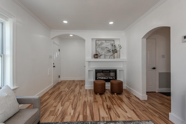 interior space with arched walkways, a glass covered fireplace, crown molding, and wood finished floors