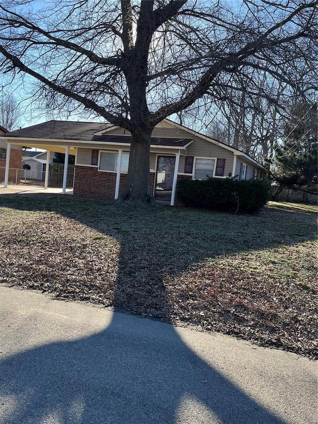 view of front of house featuring fence, a carport, and brick siding