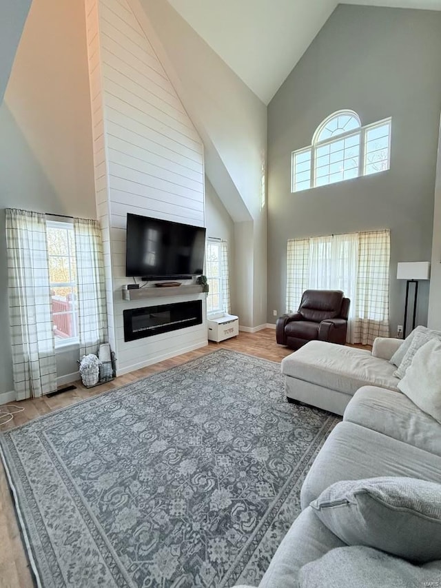 living area with baseboards, a fireplace, high vaulted ceiling, and wood finished floors