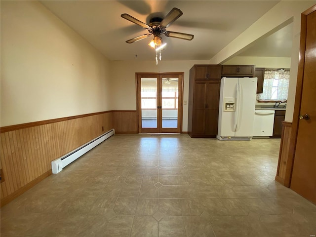 unfurnished room featuring french doors, plenty of natural light, baseboard heating, and wainscoting