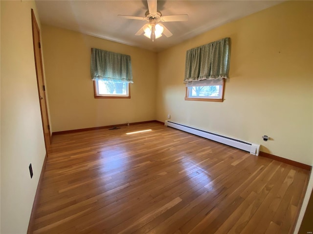 empty room featuring plenty of natural light, a baseboard heating unit, a ceiling fan, and wood-type flooring