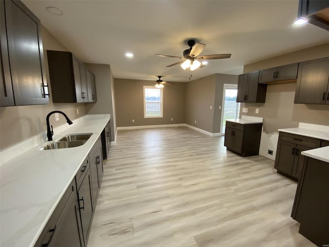 kitchen featuring light wood-style flooring, a sink, a ceiling fan, baseboards, and open floor plan