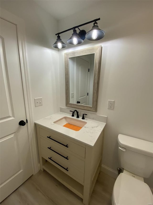 half bath with wood finished floors, vanity, toilet, and baseboards