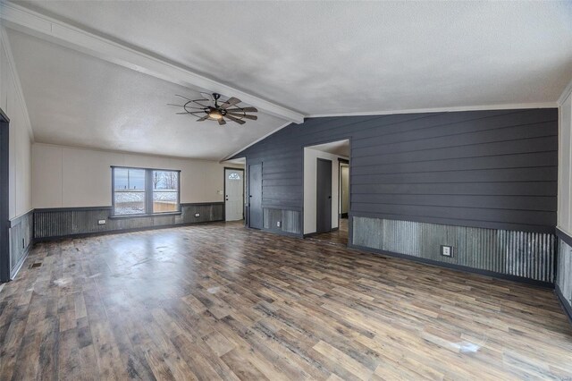 unfurnished living room featuring a ceiling fan, a wainscoted wall, wood finished floors, vaulted ceiling with beams, and a textured ceiling