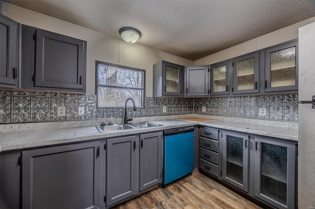 kitchen with dishwashing machine, wood finished floors, a sink, tasteful backsplash, and glass insert cabinets