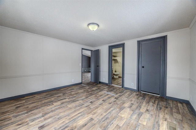 unfurnished bedroom with visible vents, connected bathroom, ornamental molding, wood finished floors, and a textured ceiling