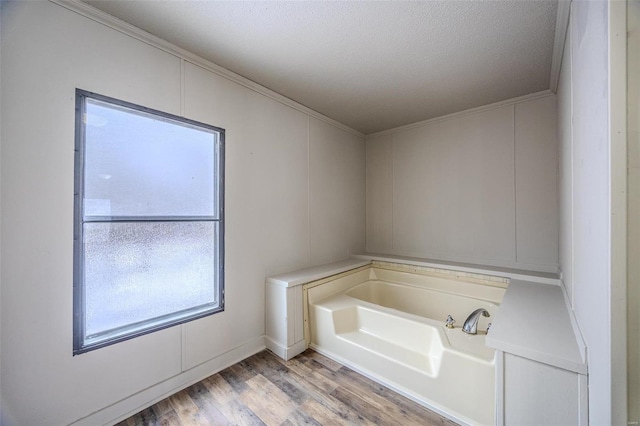 full bath with a garden tub, crown molding, a textured ceiling, and wood finished floors