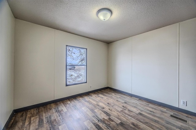 empty room with baseboards, a textured ceiling, visible vents, and wood finished floors