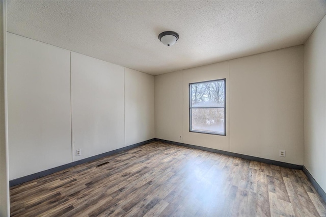 empty room with dark wood-style floors, visible vents, a textured ceiling, and baseboards