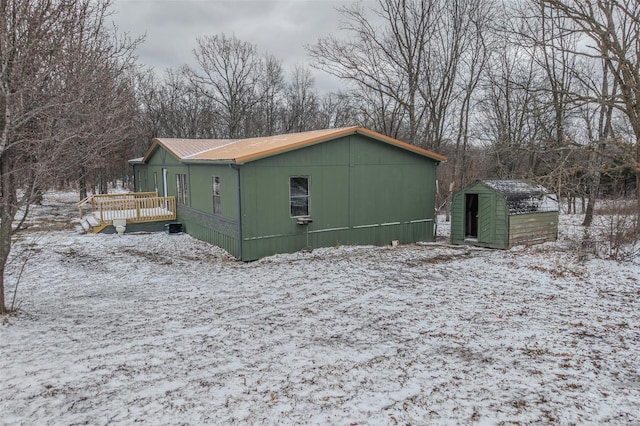 snow covered property with a shed, a deck, and an outdoor structure