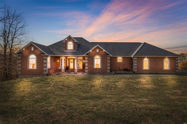 view of front facade with brick siding, a lawn, and a shingled roof