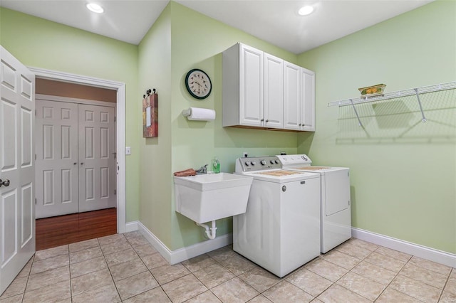 clothes washing area with washer and clothes dryer, a sink, cabinet space, light tile patterned floors, and baseboards