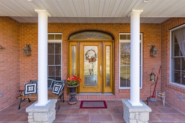 doorway to property with a porch and brick siding