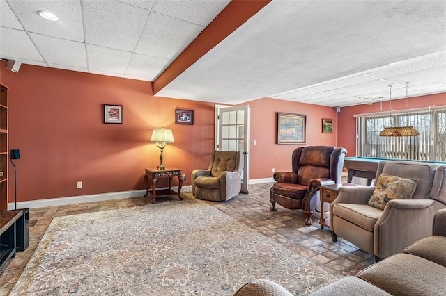 living room featuring billiards, stone tile floors, baseboards, and a drop ceiling