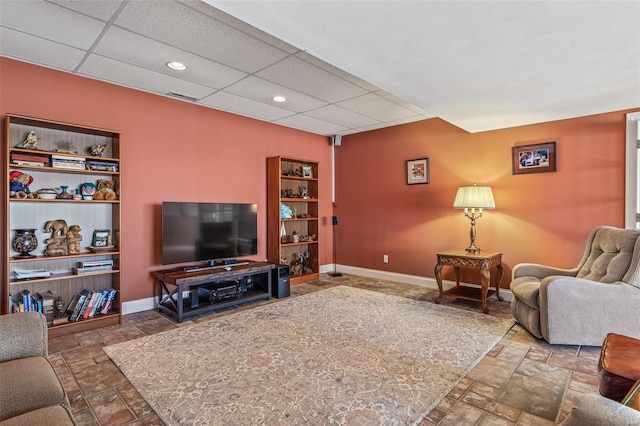 living room with stone tile floors, visible vents, a paneled ceiling, and baseboards