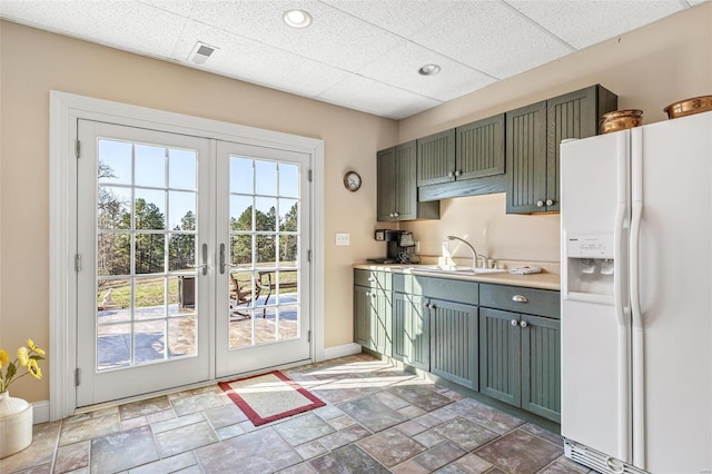 kitchen featuring baseboards, stone tile flooring, a sink, white fridge with ice dispenser, and green cabinets