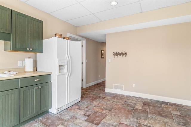 kitchen with green cabinets, white refrigerator with ice dispenser, a paneled ceiling, and baseboards