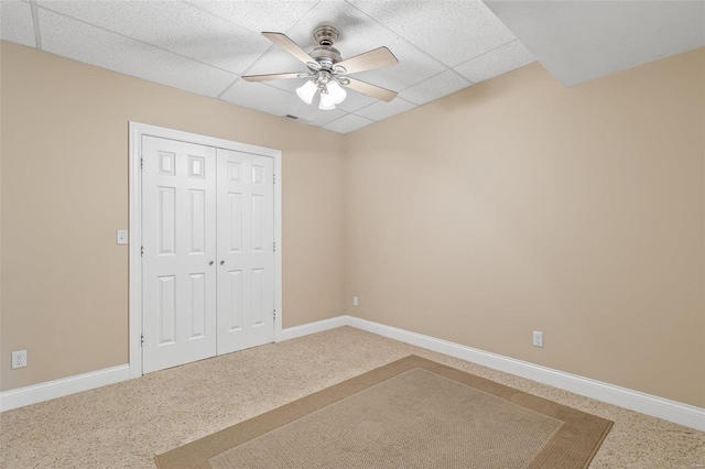 unfurnished bedroom with a paneled ceiling, a closet, baseboards, and carpet flooring