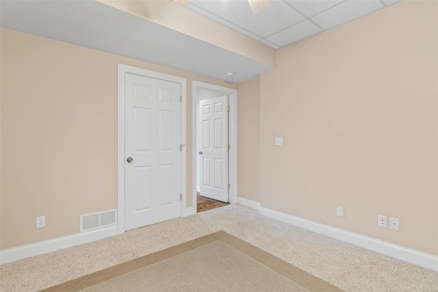 carpeted empty room with visible vents, a paneled ceiling, and baseboards