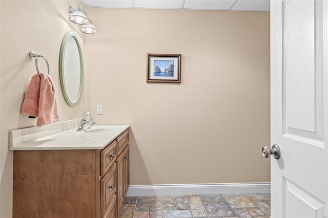 bathroom with a paneled ceiling, baseboards, vanity, and stone finish floor