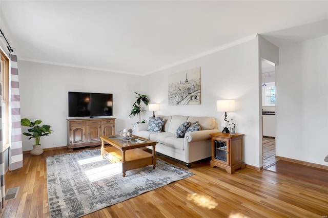 living room featuring visible vents, baseboards, wood finished floors, and crown molding