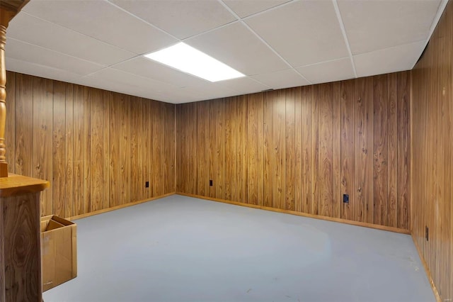 spare room with finished concrete floors, baseboards, wooden walls, and a drop ceiling