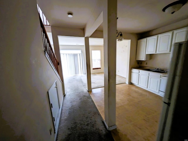 kitchen with white cabinets, light colored carpet, a sink, and freestanding refrigerator