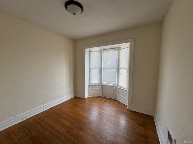 unfurnished room featuring visible vents, baseboards, and wood finished floors