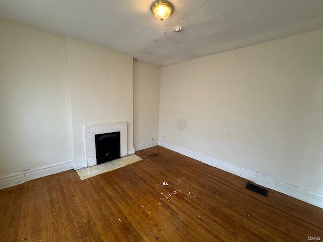 unfurnished living room with baseboards, a fireplace, visible vents, and wood finished floors