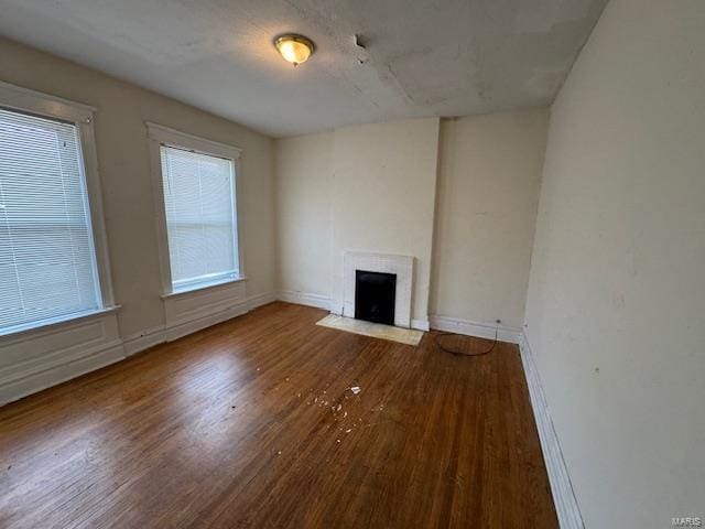 unfurnished living room featuring a fireplace with flush hearth, baseboards, and wood finished floors