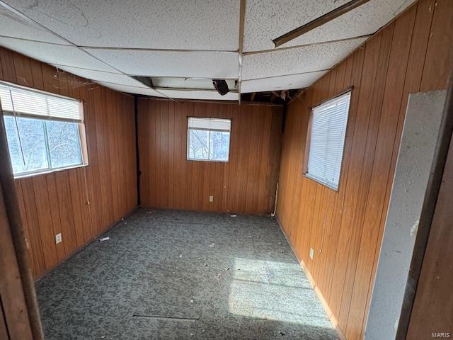 unfurnished room featuring wood walls and a drop ceiling