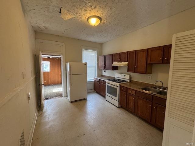 kitchen with a textured ceiling, under cabinet range hood, white appliances, a sink, and light floors