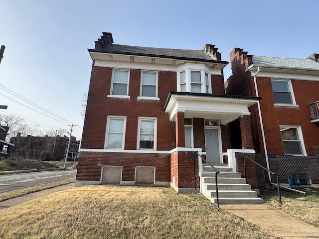 view of front of house with a porch, a front yard, and brick siding